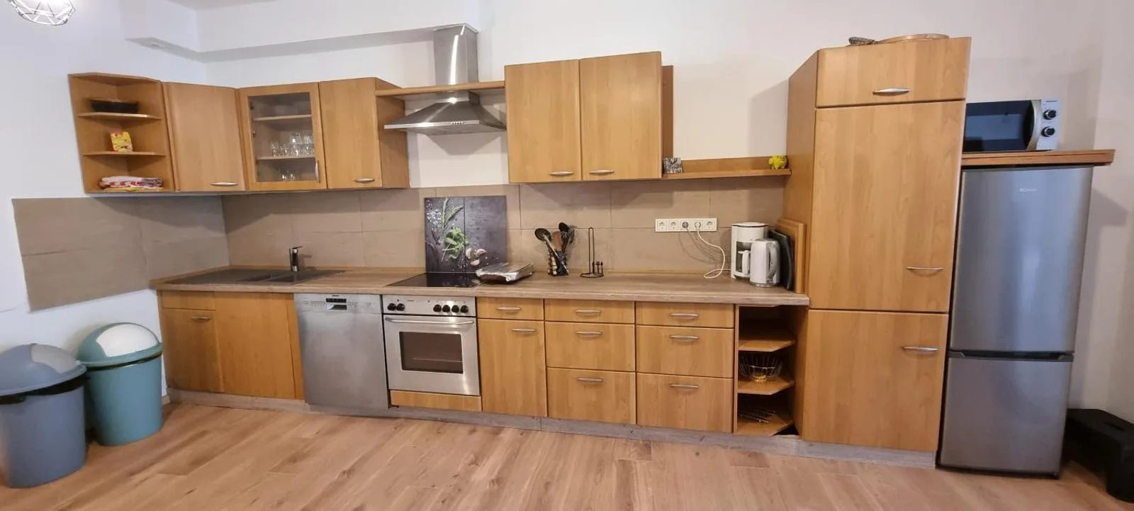 Voll ausgestattete Einbauküche in Holzoptik mit Ceranfeld, Backofen, Geschirrspüler, Kühlschrank und Dunstabzugshaube, komplette Wandlänge im Bild